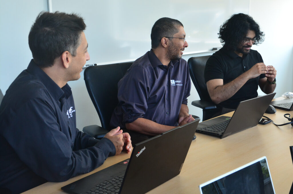 Three EMKAL technicians seated at a table in a board room working together.